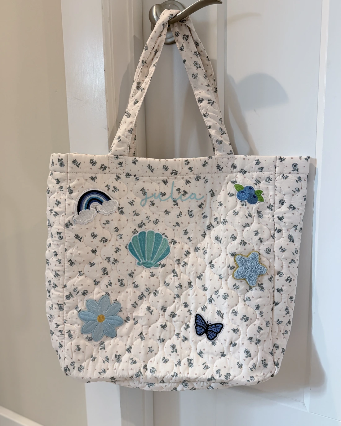 Quilted floral tote with a stitched name and chenille patches of a shell, a rainbow, a flower and a butterfly